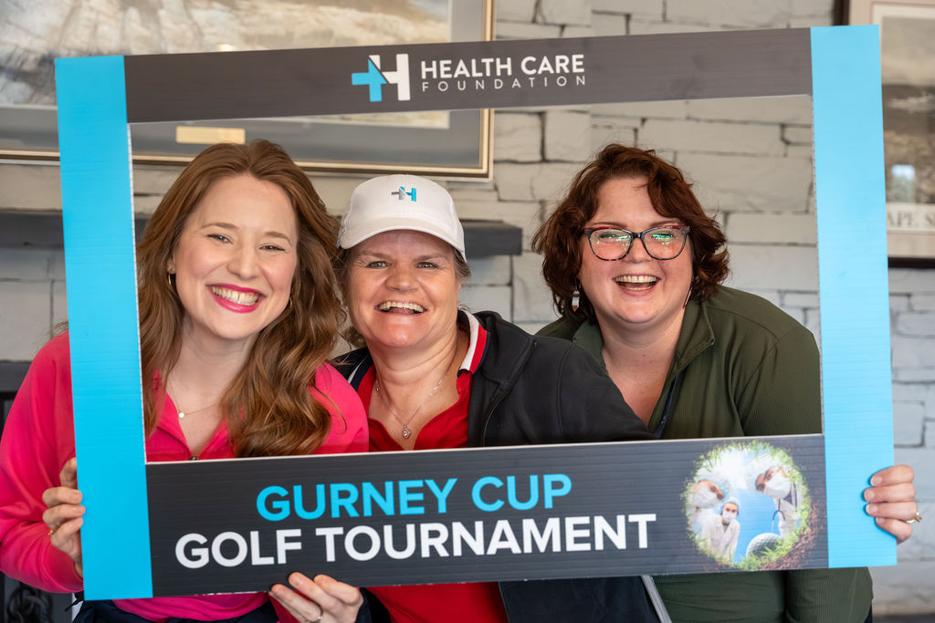 Three participants smiling in a photo frame at the 2026 Gurney Cup Golf Tournament