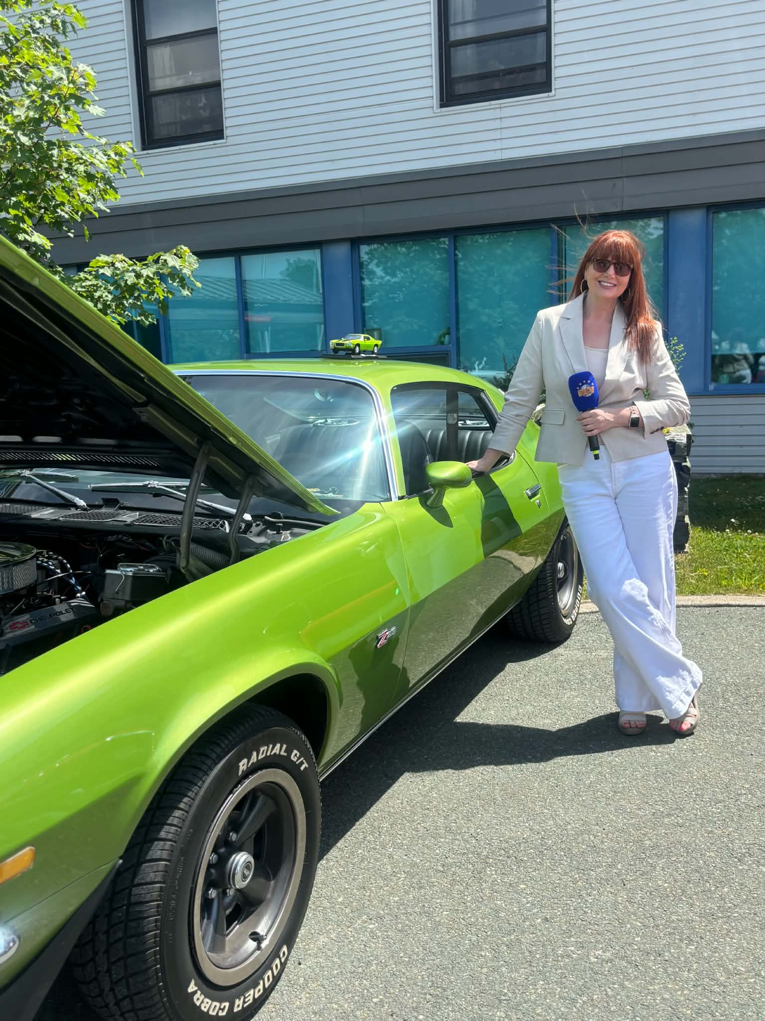 Participant beside a green muscle car with its hood open at a Health Care Foundation car show