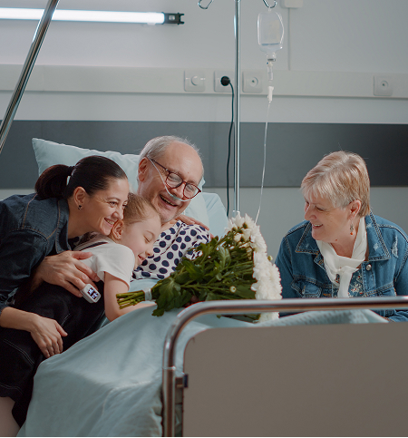 Family visiting a smiling older patient in a hospital bed