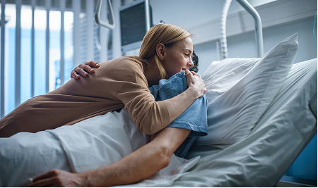 Patient resting in a hospital bed while a family member comforts them