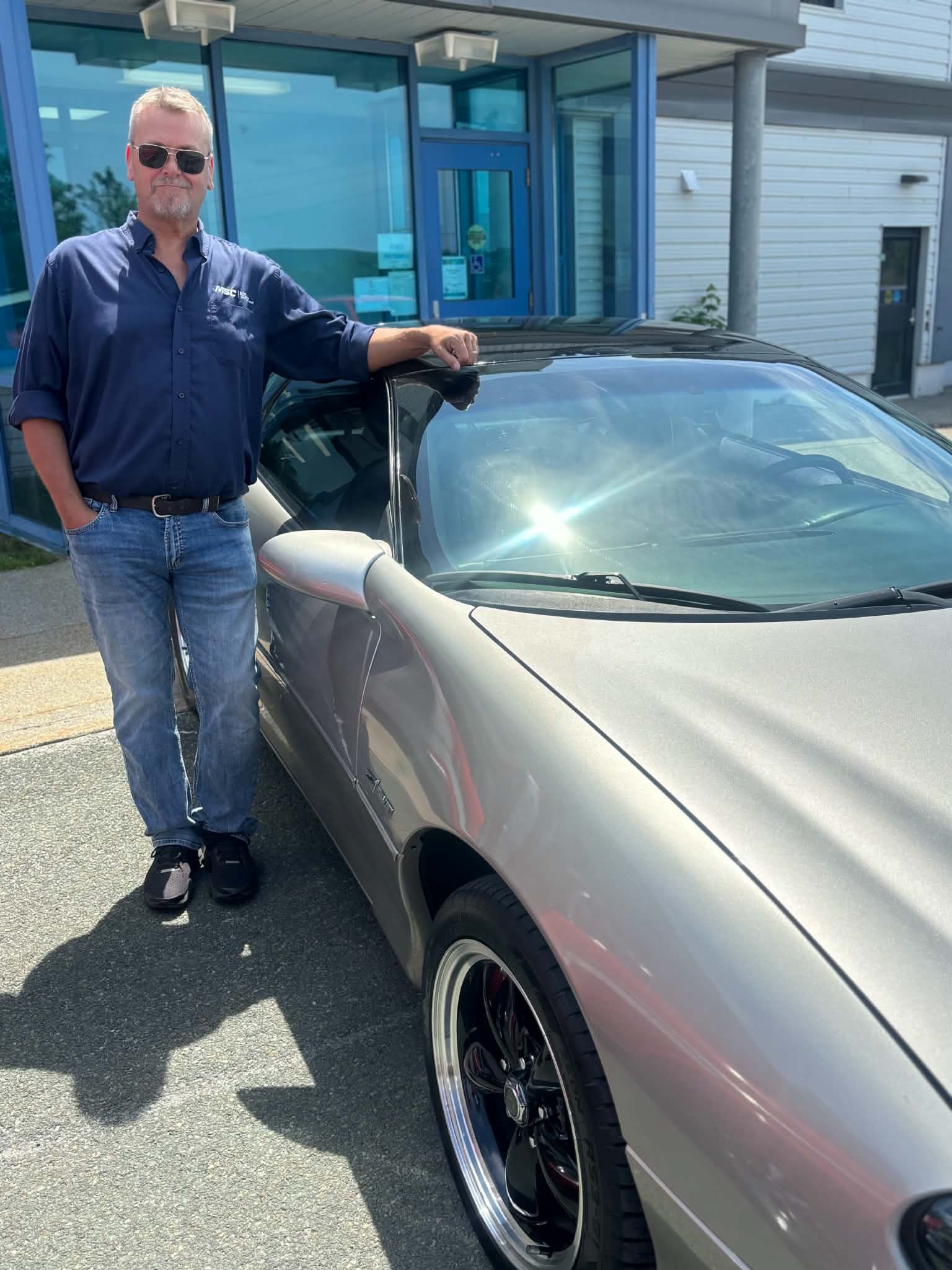 Participant standing beside a silver convertible at a Health Care Foundation car show