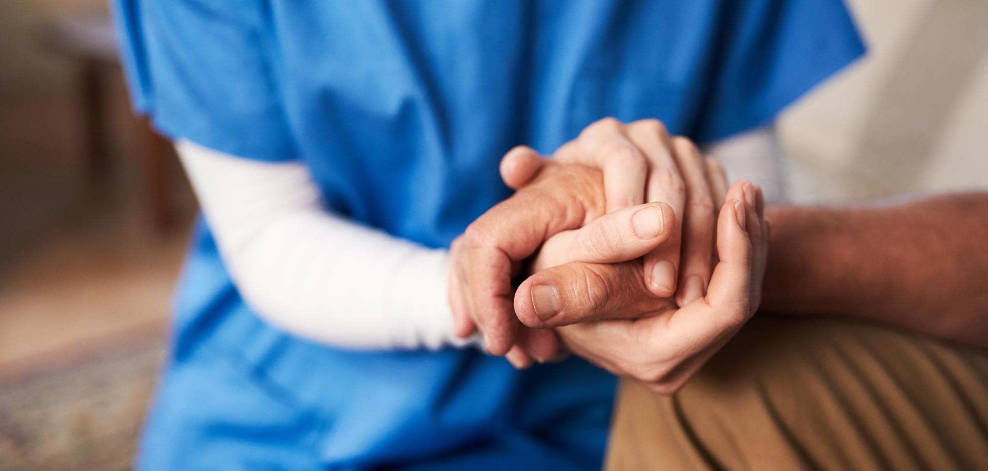 Health care worker in blue scrubs holding a patient's hands