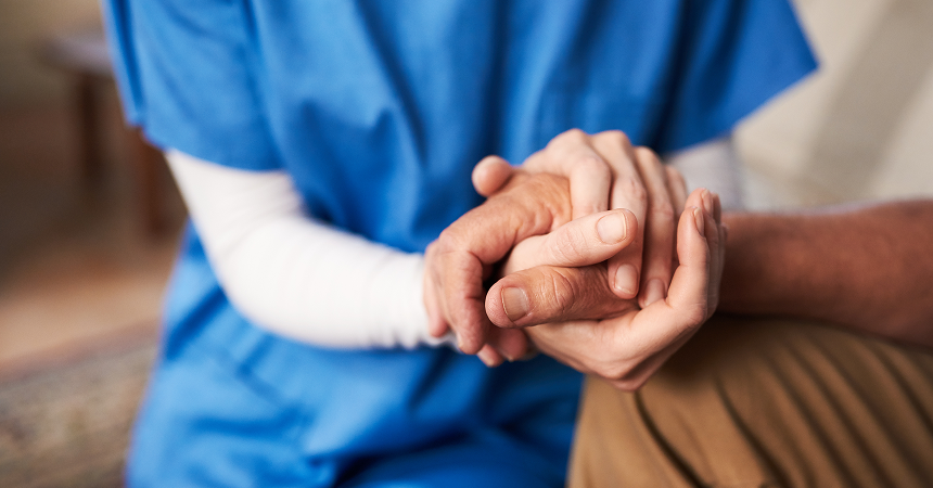 Health care worker in blue scrubs holding a patient's hands