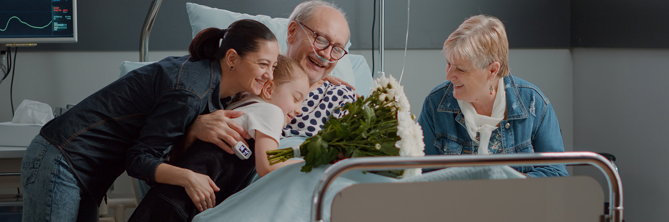Family visiting a smiling older patient in a hospital bed